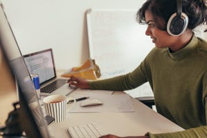 Female programmer working in office. Woman looking at laptop while coding on desktop computer.